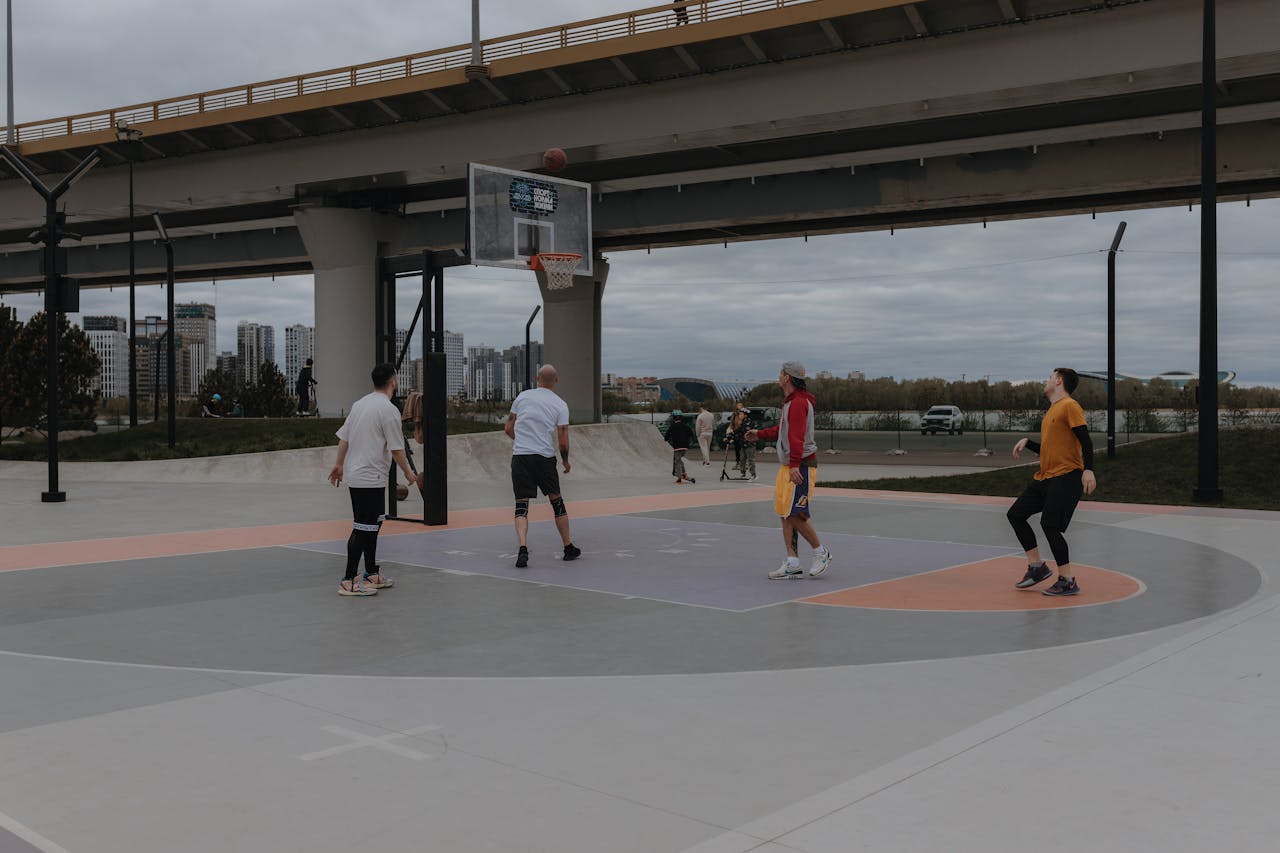 People playing basketball on a court under a bridge